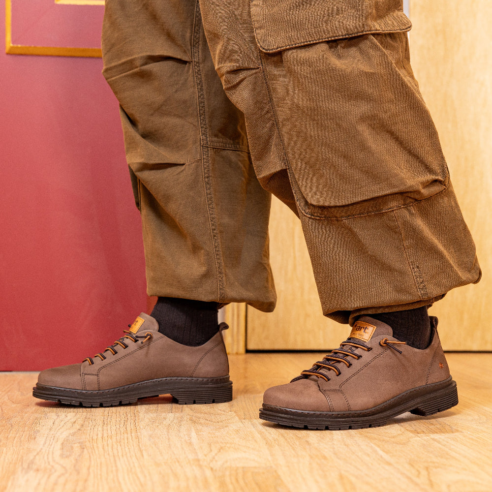 Brown shoes and cargo pants on a wooden floor with a red wall in the background