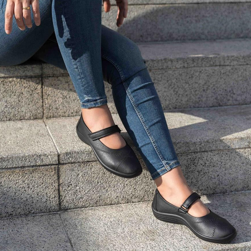 Person wearing blackArcopedico Triglav shoes and blue jeans sitting on stone steps.