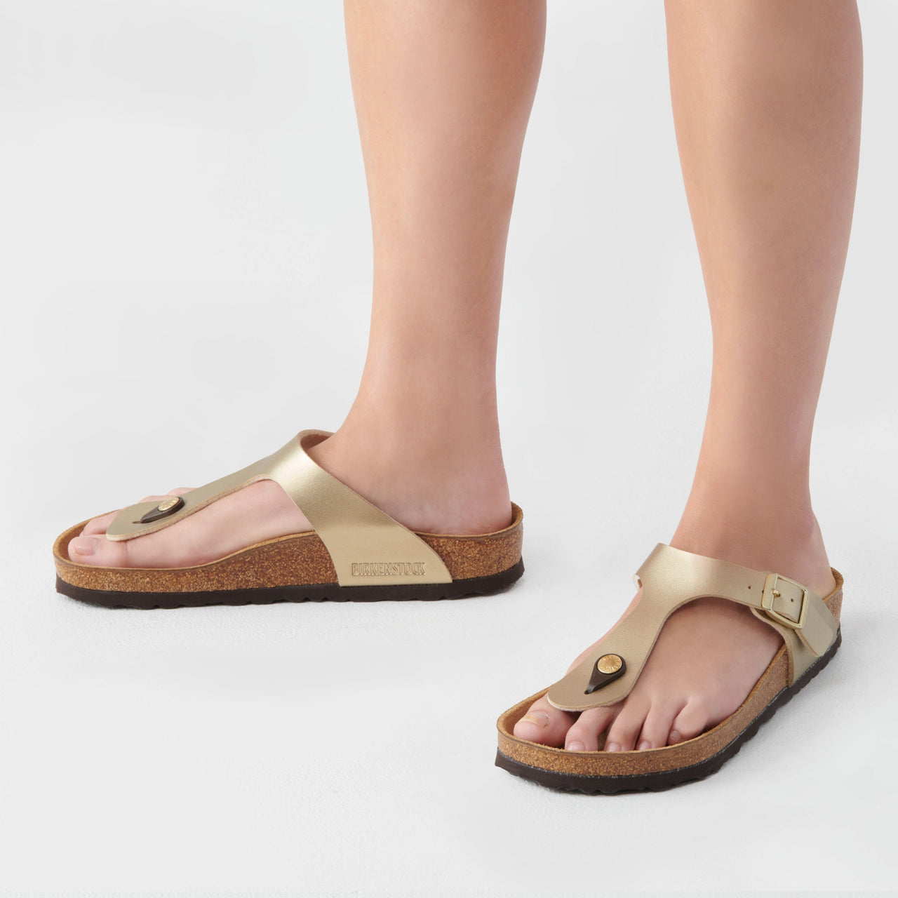 Gold sandals worn by a person on a light gray background