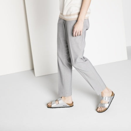 Model in grey trousers and knit top walking in silver Arizona sandals
